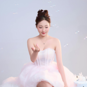 Woman wearing a blush pink strapless princess-style tulle mini dress with a sweetheart neckline and layered skirt, styled for an elegant party or special occasion.