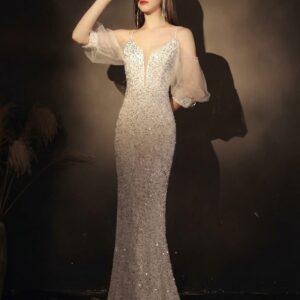 Woman wearing a champagne silver mermaid evening gown with shimmering sequins, an illusion V-neckline, sheer puff sleeves, and a floor-length silhouette for a luxurious formal occasion.